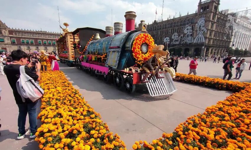 Megaofrenda in Mexico City's Zocalo square, of a parade float made to look like a steam locomotive, decorated in papel picada, Mexican marigolds and a larger-than-life figure of a Mexican revolutionary holding a gun and wearing a straw sombrero.