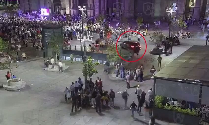 A car drives through a busy plaza in front of a cathedral, heading toward a crowd of people.