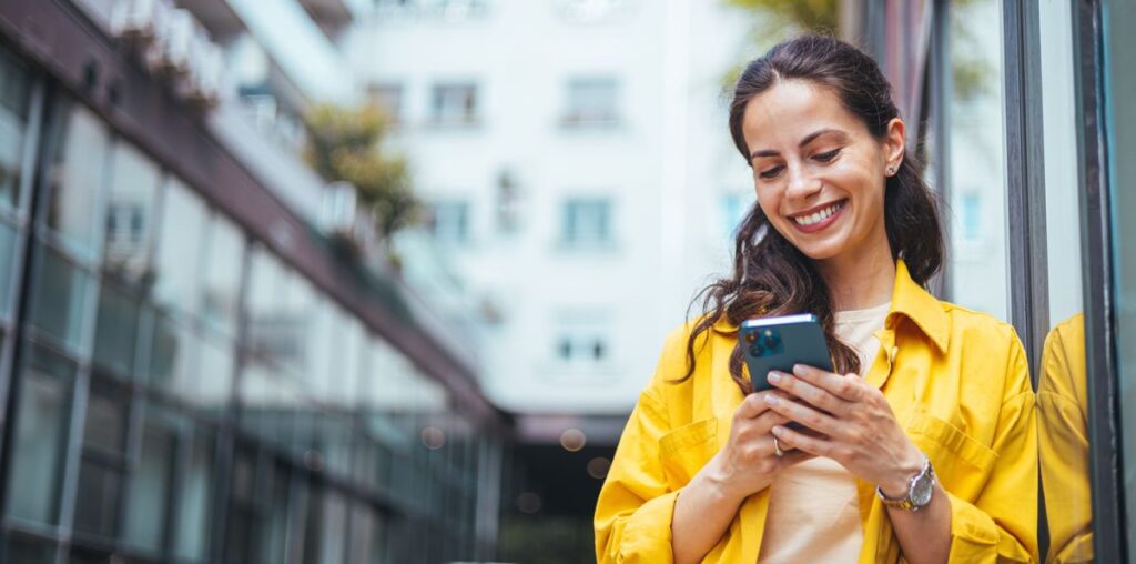 A woman by a business-looking building using a phone and smiling