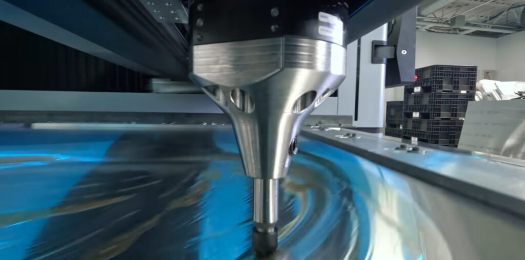 A large silver cone attached to a black hemisphere floats over a piece of sheet metal held in a metal frame. The metal has what appears to be machine grease on it to aid in the forming process.