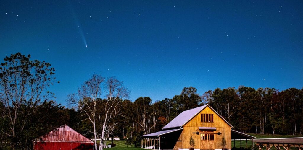 a fuzzy white streak in the night sky above a red barn