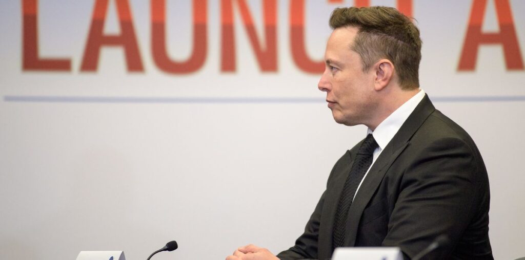 profile view of a man in a black suit, with a white wall in the background