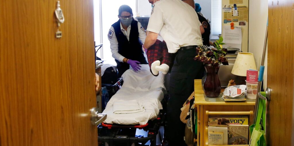 Monday, 9:23 a.m. EMT Emily Moran of Melrose and paramedic Ricky Cormio of Medford lifted an elderly patient who had a fever, a possible sign of COVID-19, onto a stretcher for transport to Mass General Hospital, their second call of the day.