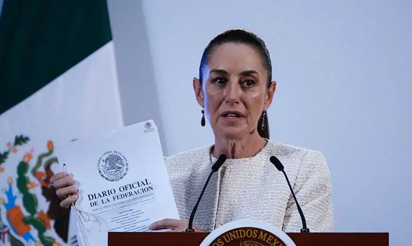 Claudia Sheinbaum at a press conference holding a copy of Mexico's Official Gazette of the Federation document