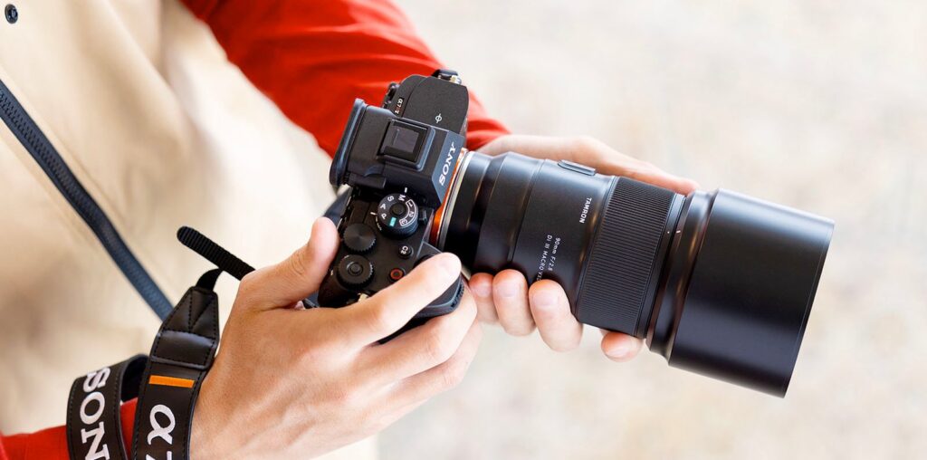 A person holding a Sony camera with a large lens, adjusting settings while wearing a camera strap labeled "Sony α7.