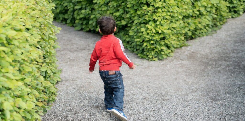 A boy turns to take a path in a maze.