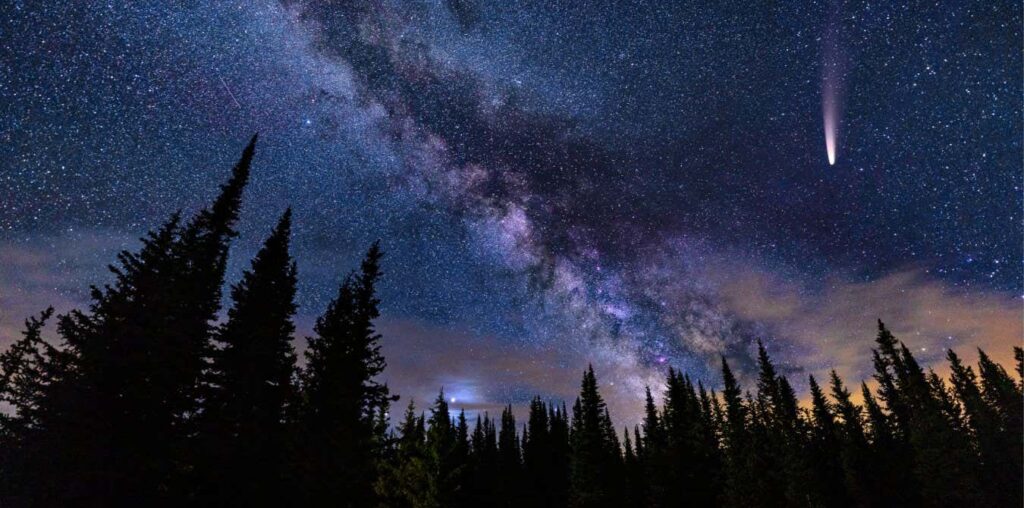 NEOWISE Comet in Night Sky with Milky Way Galaxy - Bright rare comet in dark sky with crisp bold Milky Way Galaxy and silhouetted trees mountain astrophotography landscape. Very dark skies perfect for stargazing.