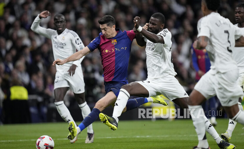 Penyerang Barcelona Robert Lewandowski berebut bola dengan pemain Real Madrid pada pertandingan sepak bola La Liga Spanyol di stadion Santiago Bernabeu di Madrid, Spanyol, Ahad (27/10/2024). Barcelona berhasil menaklukkan Madrid dengan skor telak 4-0. Robert Lewandowski mencetak dua gol di menit 54 dan 56. Sedangkan dua gol lainnya dicetak Lamine Yamal menit ke-77 dan Raphinha menit ke-84.