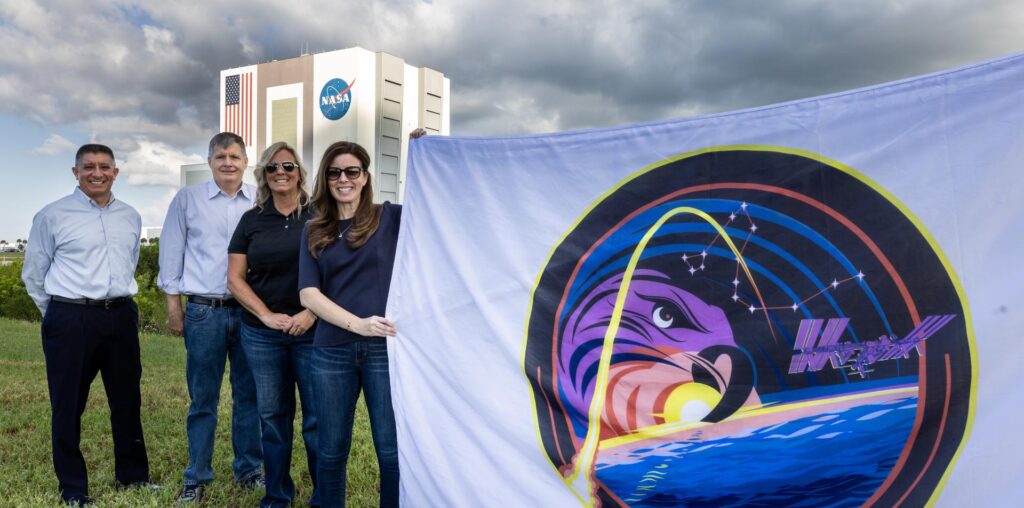 From left, Richard Jones, CCP (Commercial Crew Program) deputy program manager at NASA’s Johnson Space Center in Houston; Steve Stich, program manager for CCP; Dana Hutcherson, CCP deputy program manager at NASA’s Kennedy Space Center in Florida; and Diana Oglesby, director, Strategic Integration and Management Division, Space Operations Mission Directorate, pose with the agency’s SpaceX Crew-9 mission flag near the countdown clock at the NASA News Center at the Kennedy on Tuesday, Sept. 24, 2024.