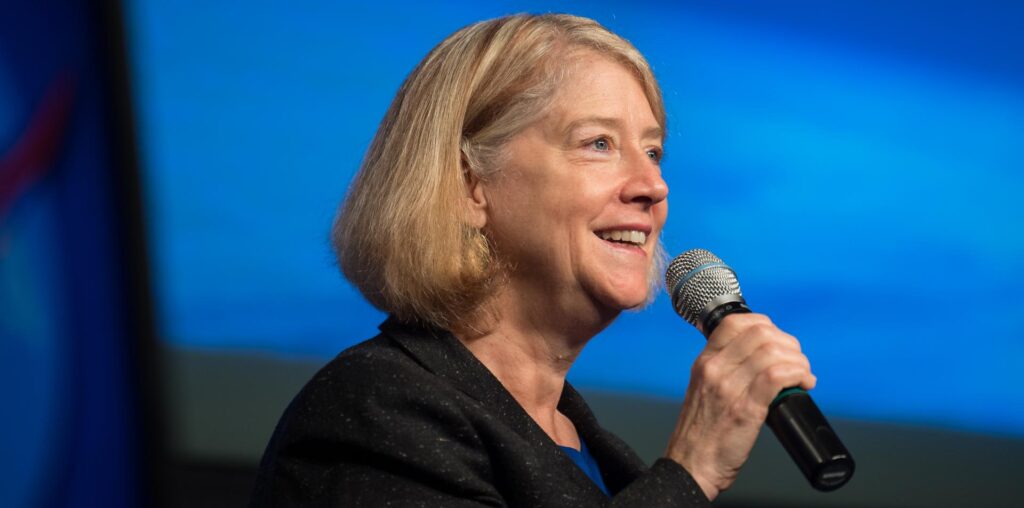 NASA Deputy Administrator Pam Melroy smiles as she speaks into a microphone at an employee town hall, with a blue background behind her.