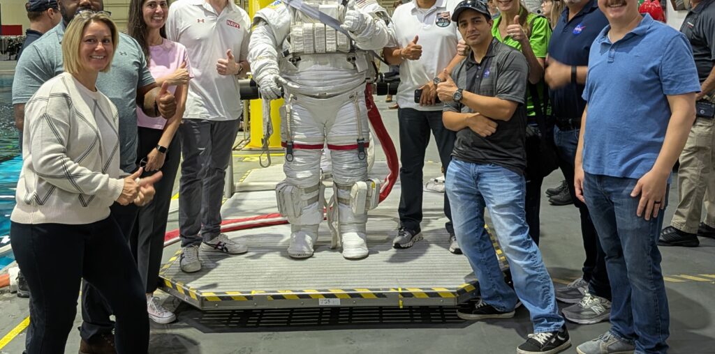 Group photo of NASA SkillBridge employees around an Astronaut suit at the JSC Neutral Buoyancy Laboratory.