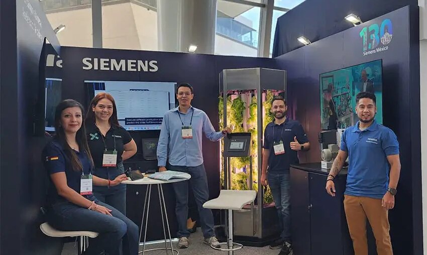 Young Siemens Mexico employees smile and pose for a photo with a tank full of experimentally grown lettuce