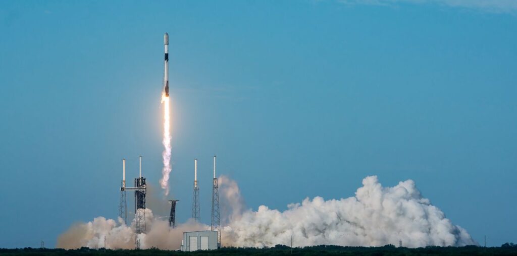 a black-and-white spacex falcon 9 rocket launches into a blue sky.