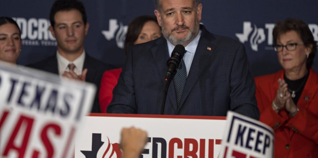 Ted Cruz stands in front of a microphone surrounded by supporters and Ted Cruz signs