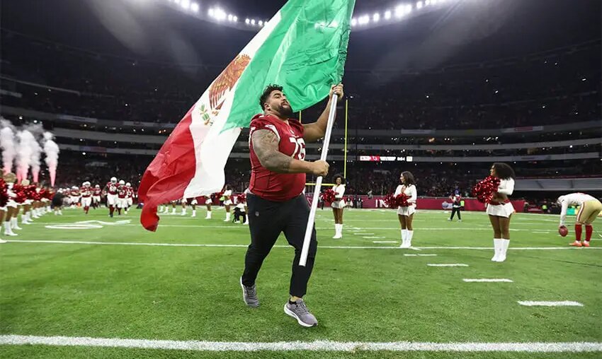 A football player runs with a Mexican flag across the field of Mexico City's Aztec Stadium