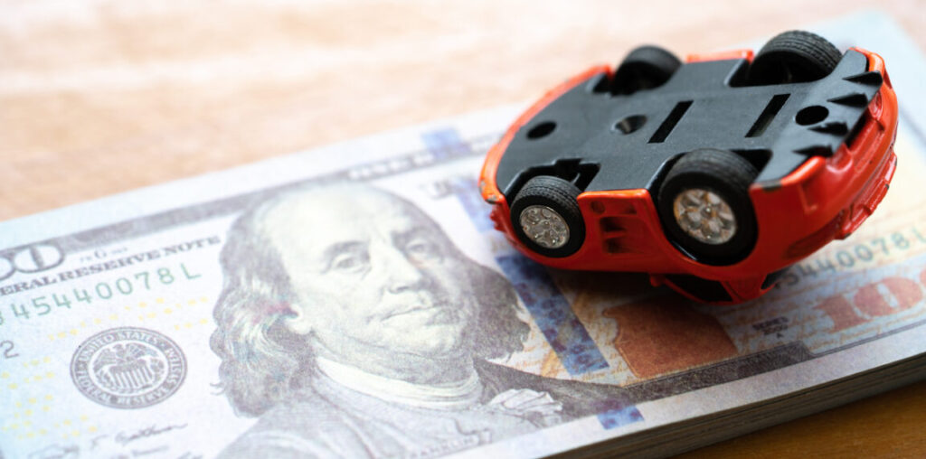 An upside-down toy car on a stack of $20 bills