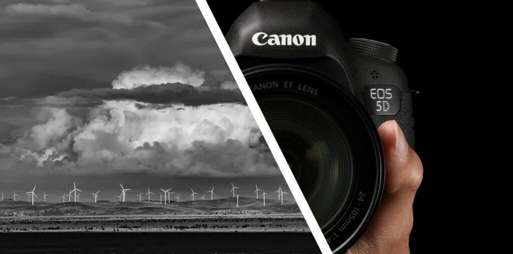 Monochrome image of a distant wind farm alongside a Canon DSLR camera in the hand with black background